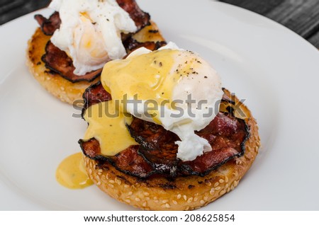 Benedict eggs with crispy bacon and hollandaise sauce on toasted Maffin on clean plate