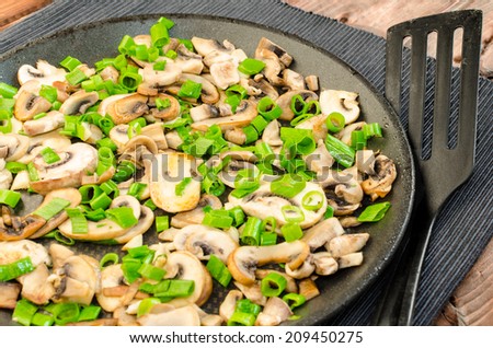 Fried mushrooms with spring onion on pan, wood table