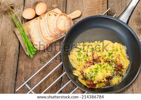 Omelet with bacon and cheese, home bread and chive on top, on frying pan