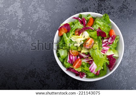 Fresh mixed salad with endive and cherry tomatoes on black plate dining, pouring olive oil