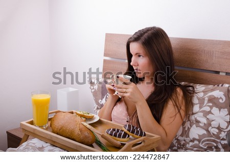 Beautiful young woman eating breakfast in bed in the morning, complete breakfast
