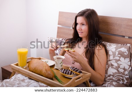 Beautiful young woman eating breakfast in bed in the morning, complete breakfast spread butter