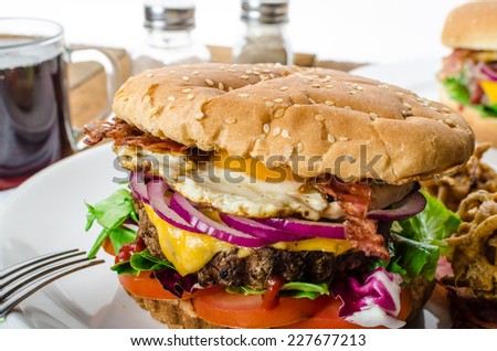 Beef burger with red onion and fried egg, crispy bacon and salad, onion bhajis