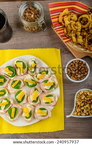 New Year\'s Eve meal - canapes with ham, cheese and spinach leaves, spicy cheese balls (Aigrettes), onion rings, roasted nuts with thyme and olive oil and beverages