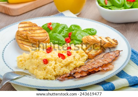 Scrambled eggs English style, bacon, fresh salad of spinach and microgreen, chilli pepper, orange juice