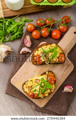Scrambled eggs on toasted bread with bacon, herbs and tomato poached in balsamic reduction