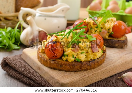 Scrambled eggs on toasted bread with bacon, herbs and tomato poached in balsamic reduction
