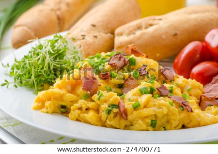 Scrambled eggs with bacon, chive and tomatoes, fresh juice and little microgreens healthy salad
