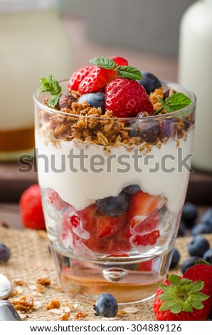 Yogurt with baked granola and berries in small glass, strawberries, blueberries. Granola baked with nuts and honey for little sweetness. Homemade yogurt