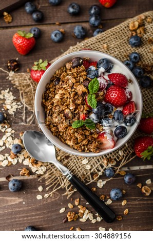 Yogurt with baked granola and berries in small bowl, strawberries, blueberries. Granola baked with nuts and honey for little sweetness. Homemade yogurt