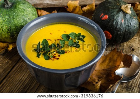 pumpkin soup with chilli and herbs, nice autumn leaves and rustic wood table