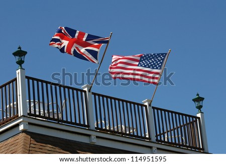 An American and British flag waving in the wind on a rooftop deck