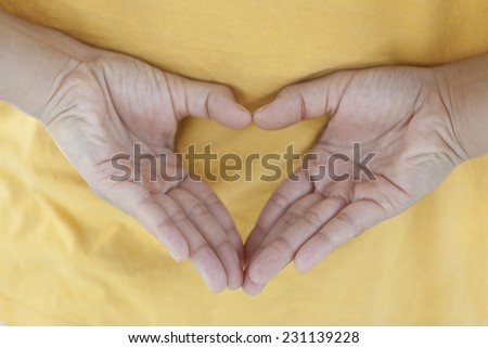 Closeup of female hands on back of she in yellow shirt. She showing making heart shape love fall in love secret symbol.