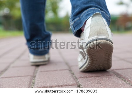 Teenager walking in sport shoes on pavement at summer day