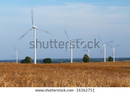 Power generating wind turbines on cultivated wheat field, blurred to show quick movement, Poland