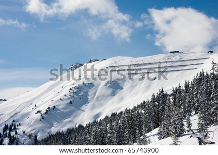 Alps mountains and forest covered by snow and sport resort center buildings in background