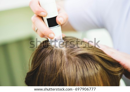 Hair doctor checking hair. Diagnostics hair and scalp.Trihoskopiya. Doctor examine patient female hair a special apparatus