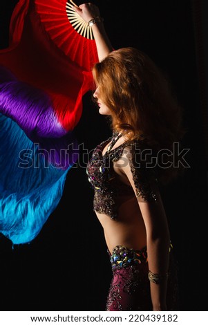 woman in carnival costume with a fan on black. belly dance