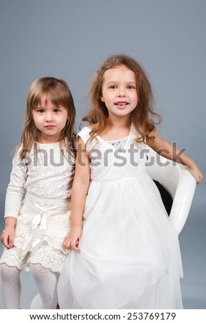 Two little funny and laughing girl in white clothes stand and hold hands.
