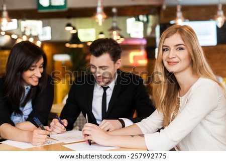 Group of 3 young business people gathered together at a table discussing an interesting idea in the cafe