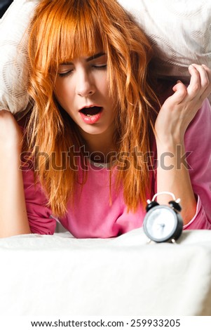 alarm clock. Young woman in the background covering ears with pillow. room clock bed lazy sleep wake alert