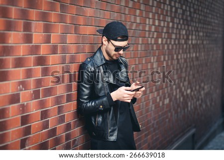 Typing text message. handsome young man in smart casual wear holding mobile phone while leaning at the brick wall