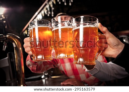 Happy friends clinking with beer mugs in pub,