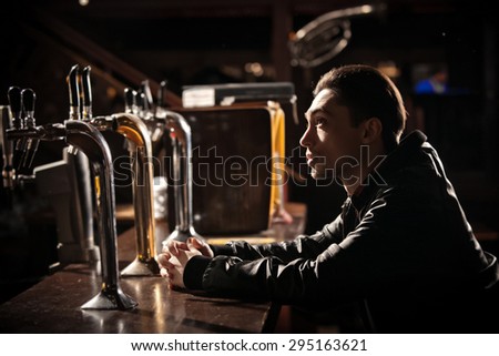 It was a hard day. Depressed young man drinking beer in bar and holding hand in hair