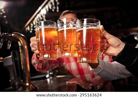 Happy friends clinking with beer mugs in pub,