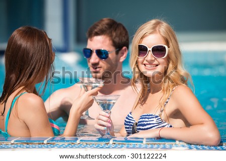 Good looking guy flirting with two women at the swimming pool, drinking cocktails