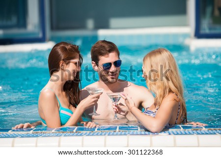 Good looking guy flirting with two women at the swimming pool, drinking cocktails