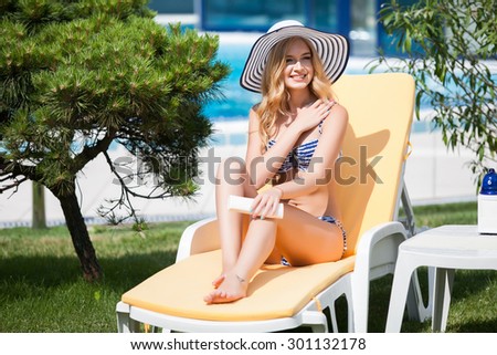 Beautiful happy woman in black bikini applying sun block cream on the tanned body.