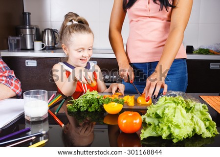 little girl cutting vegetables with her mother in the kitchen
