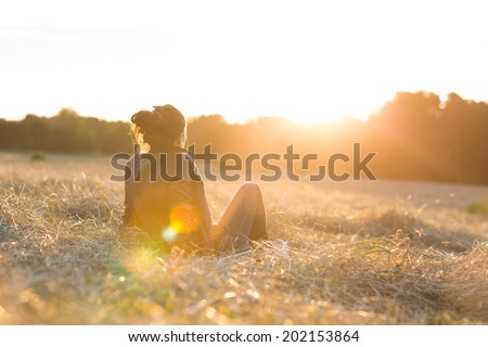 Portrait of a beautiful young woman or girl on meadow watching the sunset enjoying nature summer evening outdoors. Soft red light. Sunshine.