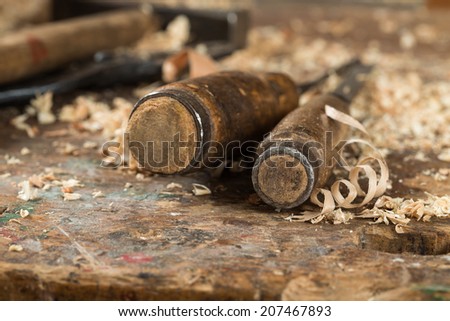 Composition of two antique chisels and wood chips on the working desk in wood workshop.