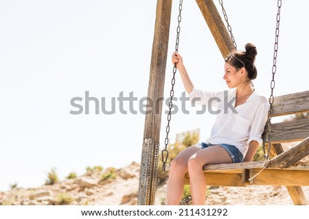 Young black hair woman sitting on the swing in the desert background. Low depth of field. Attractive girl looking out over a dramatic valley in the Negev desert in Israel.
