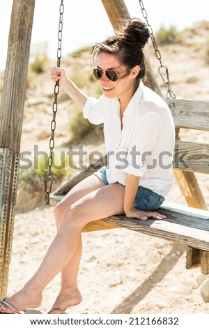 Young black hair woman sitting on the swing in the desert background. Low depth of field. Attractive girl looking out over a dramatic valley in the Negev desert in Israel.