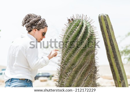 Beautiful girl in white shirt, sunglasses and scarf standing and touching cacti.