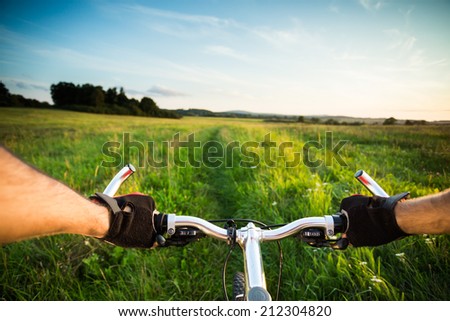 Man biking fast. View from bikers eyes. The end of the road and start of the track. Beautiful bright sunset light over the countryside with blue sky.