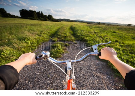 Wide shot of retro orange bicycle at sunset in countryside. Active summer. Woman biking in meadow at sunset. View from bikers eyes.