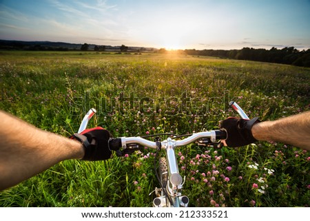Man biking in meadow at sunset. View from bikers eyes. The end of the road and start of the track.