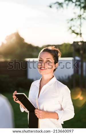 Young happy businesswoman or landscape architect speaking with her client. Young professional is dressed in casual clothes. Strong sunset backlit.
