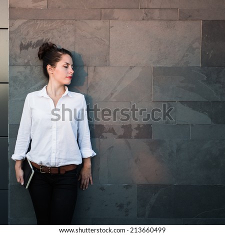 Tired happy businesswoman, architect or creative person in white shirt resting after work, leaning on the warm wall from dark stones. Delicate red evening light.