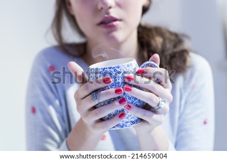 Young woman in grey sweater with red spots holding decorative cup of tea or coffee with smoke. Color toned image. Cold filter.
