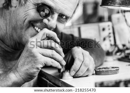 Clockmaker repairing wrist watch and smiling to the camera. Black and white photography.