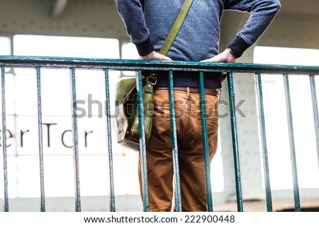 Unusual view of a man standing and leaning the railing with his bag in the train station. Color toned image. Selective focus.