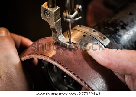 Sewing process of the leather belt. Man's hands behind sewing. Leather workshop.