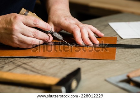 Working process of the leather wallet in the leather workshop. Woman\'s hands holding crafting tool and iron ruler.