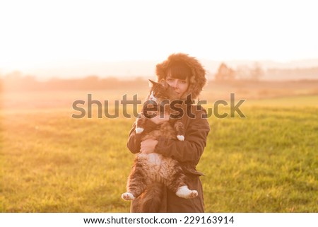 Portrait of young woman with her Norwegian Forest cat in meadow at sunset. Soft light.