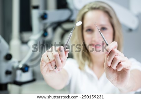 Portrait of young dentist in the cabinet. Image of dentist woman holding dentistry tools in hands. Low depth of field. Color toned image.